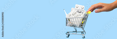 Side view of a woman hand pushing and rolling a mini shopping cart full of pills. The concept of online shopping medicine on blue background. Online Pharmacy. health insurance. Banner. Space for text