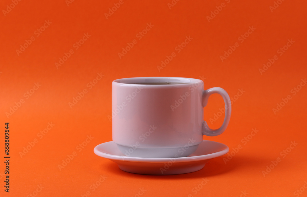 a white ceramic cup with black tea on orange background. minimalism style a white ceramic cup with black tea on orange background. minimalism style