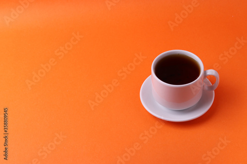 a white ceramic cup with black tea on orange background. minimalism style