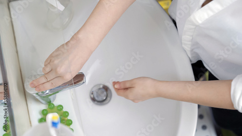 Caucasian woman switches on water tap to wash hands. Close up shot of female hands or arms washing in bathroom. High angle view. © Svyatoslav Lypynskyy