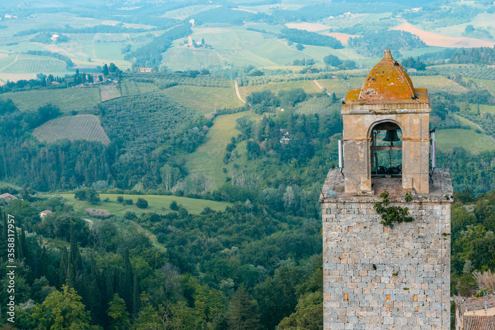 The top of Torre Rognosa with typical Tuscan countryside in the background seen from the top of the Great Tower (Torre Grossa), San Gimignano, Italy.