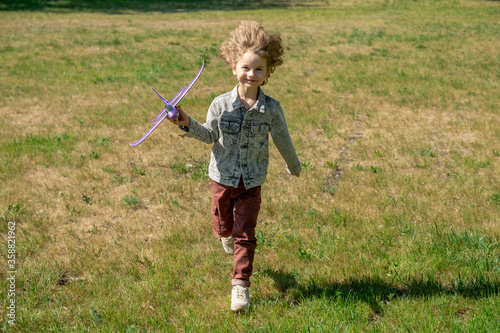 Happy cute little boy with blond curly hair holding toy airplane and running