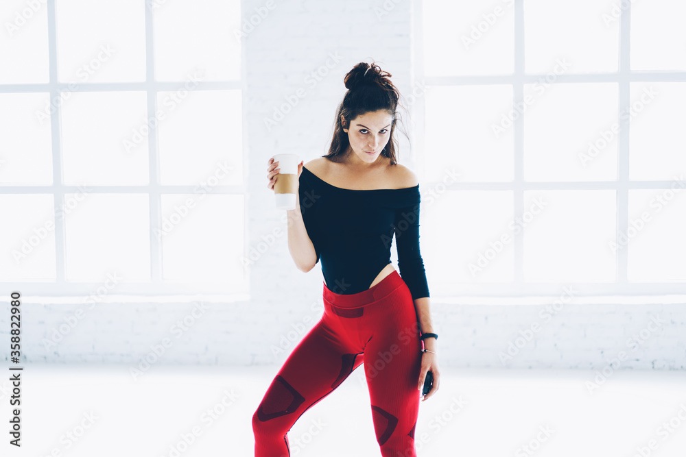 Half length portrait of motivated sports women in trendy active wear having break for drinking water on training,serious female satisfied with hard workout looking at camera holding cup with beverage Half length portrait of motivated sports women in trendy active wear having break for drinking water on training,serious female satisfied with hard workout looking at camera holding cup with beverage