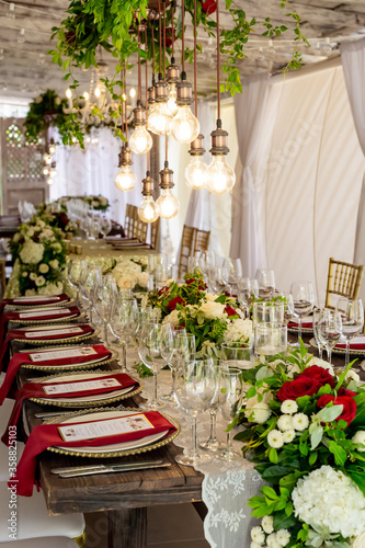 Table setting served and decorated for party event with plates, glasses, candles, napkins, lamps, flowers and invitations. Guests table, Wedding reception, Birthday, anniversary. Holiday evening