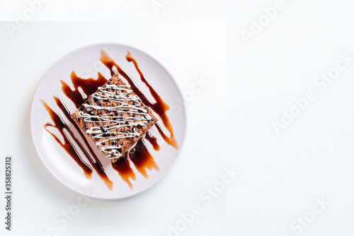 Vista superior de um bolo de chocolate brownie coberto com uma calda de chocolate servido em um prato rosa sobre um fundo branco com copyspace para textos. photo