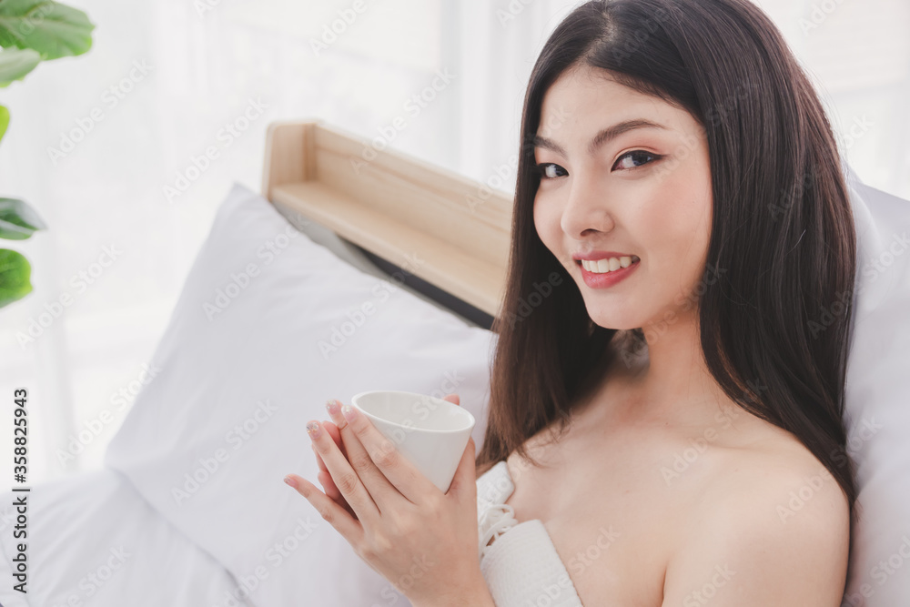 Asian beautiful girl Take a cup of coffee Have a smile Happily on white bed on a holiday. Relax and hobby time Asian beautiful girl Take a cup of coffee Have a smile Happily on white bed on a holiday. Relax and hobby time