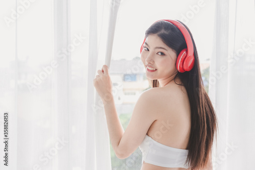Asian beautiful girl wearing red headphones and playing smartphone in happily in room