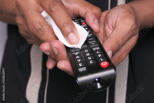man hand cleaning TV remote controller with disinfectant wet wipe