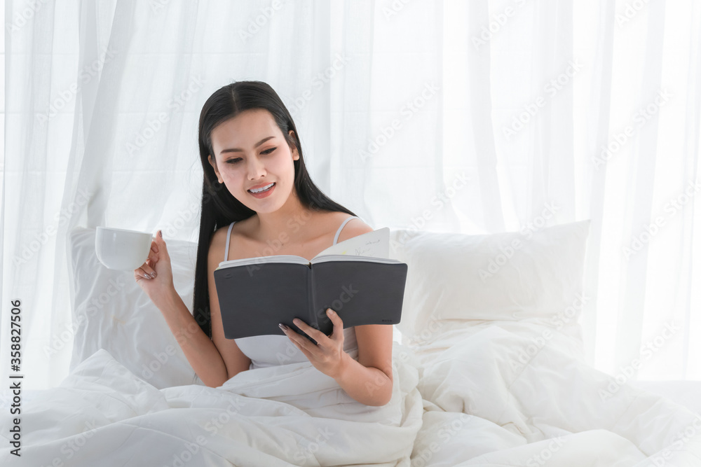 Asian girl cute and beautiful Reading a book and holding a coffee cup on bed in happy, Relax time or Work for home. Asian girl cute and beautiful Reading a book and holding a coffee cup on bed in happy, Relax time or Work for home.
