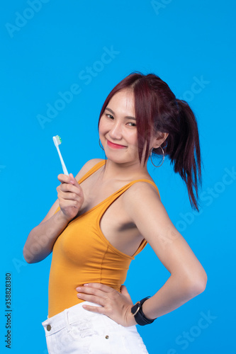 Beauty portrait young asian woman holding toothbrush and smiling on blue background. Concept good oral and dental health.