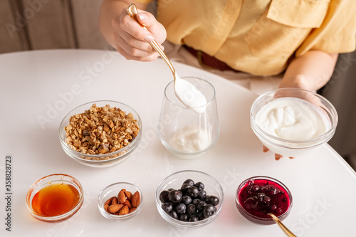 Young woman making yoghurt with honey  berries  jam and almond for breakfast