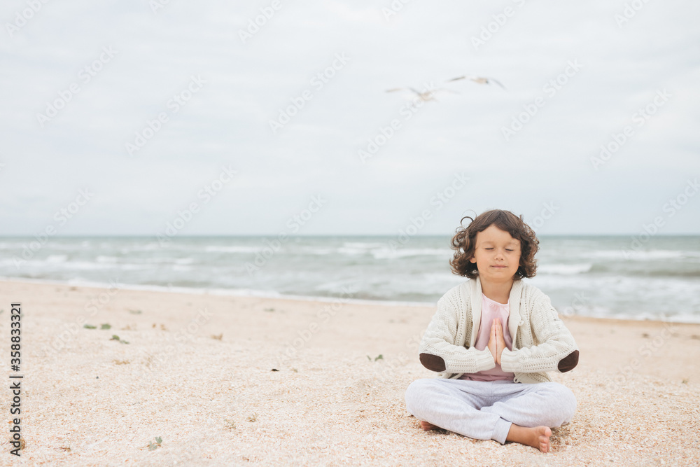 Young caucasian girl meditate at the beach, doing yoga lotus pose, child meditation outdoors