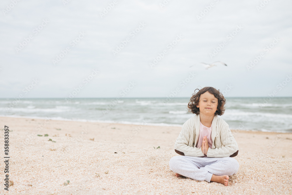 Young caucasian girl meditate at the beach, doing yoga lotus pose, child meditation outdoors