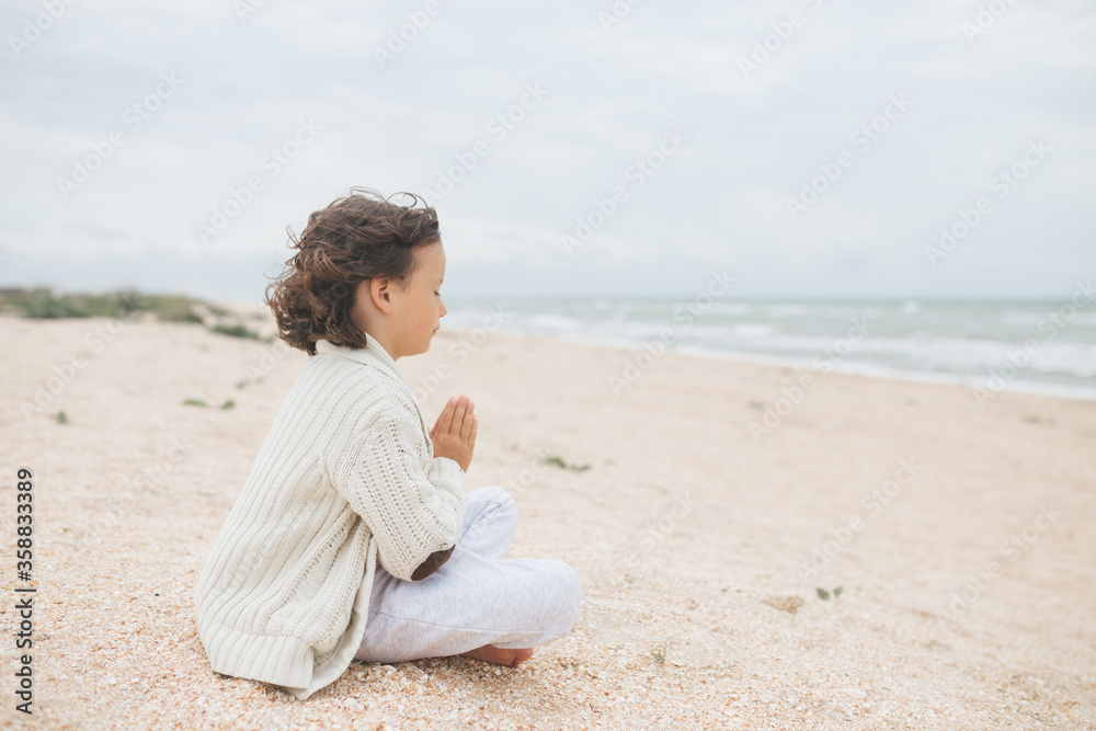 Young caucasian girl meditate at the beach, doing yoga lotus pose, child meditation outdoors
