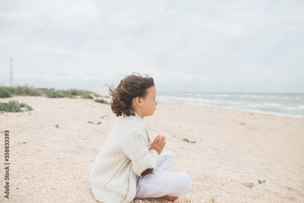 Young caucasian girl meditate at the beach, doing yoga lotus pose, child meditation outdoors Young caucasian girl meditate at the beach, doing yoga lotus pose, child meditation outdoors