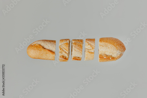 A flat lay of a baguette bread cut up on a light pastel grey background
