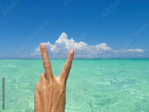 Hand of a white woman with peace sign, in the background the turquoise and transparent water of the Caribbean sea, Mexico