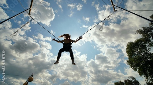Fotografie, Tablou Teenage girl silhouette jumping on the trampoline bungee jumping.