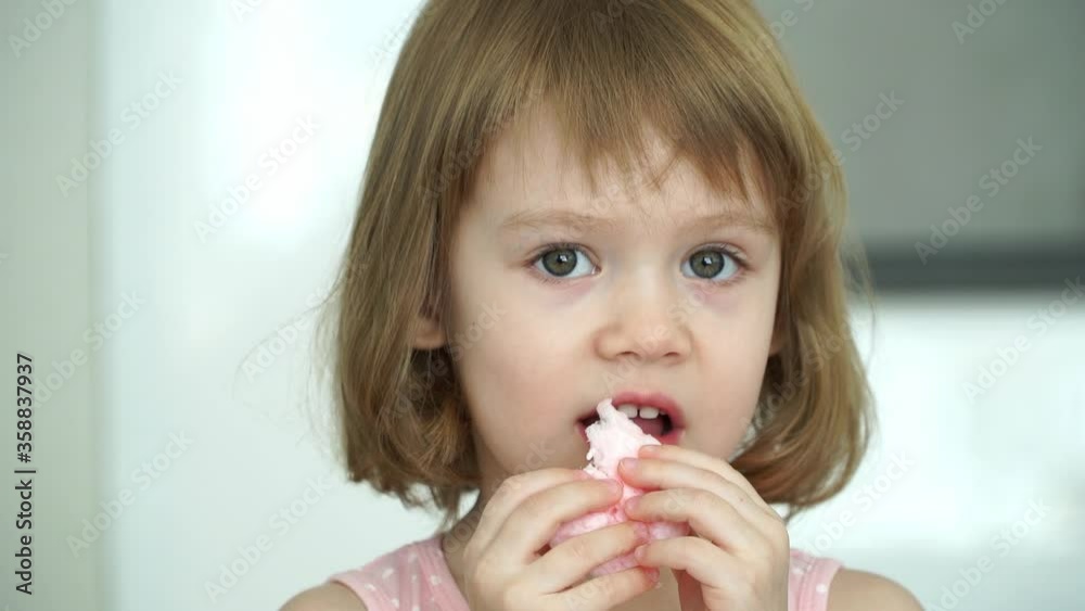 Close up of little cute 3 years old child girl eats with pleasure pink cotton candy, looks at camera, smiles and laughs. Sweet kids food concept Close up of little cute 3 years old child girl eats with pleasure pink cotton candy, looks at camera, smiles and laughs. Sweet kids food concept