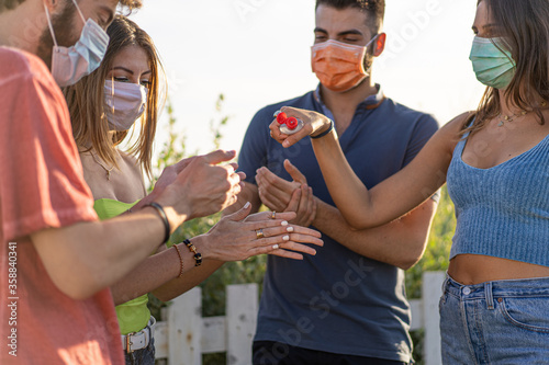 Group of young friends wearing protective masks using sanitizing gel together against the coronavirus (COVID-19) pandemic.