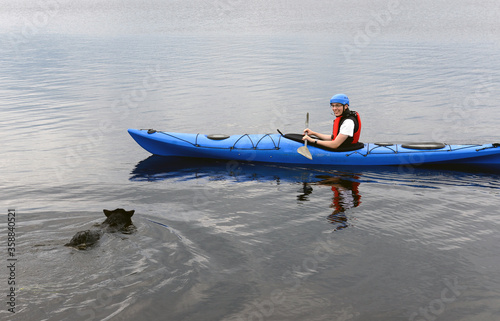 Young man kayaking with dog on big forest lake. Finnish Lapland