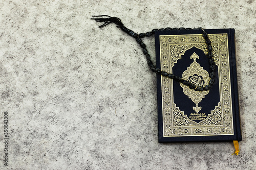 Holy Quran with Arabic calligraphy meaning of Al Quran and black rosary