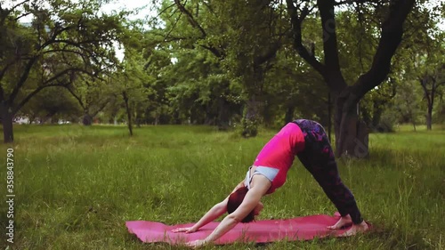 Yoga girl practicing one-legged downward-facing dog exercise outdoors in the park or garden. Maintaining flexibility and stability in the hip joints is crucial for lower-back health. Prores 422.
