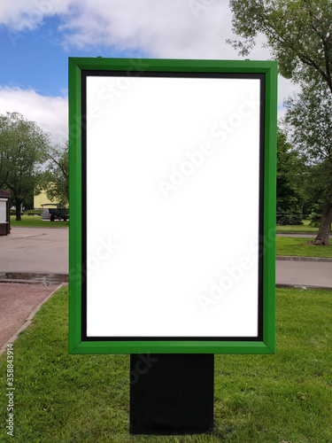 A green information stand with place for text stands in a summer park.