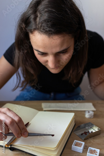 Young woman holding a precious stone with jewelry tweezers in her workspace. Portrait of a gemologist.