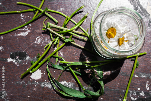 Chamomile flowers in a glass jar and green grass on a wooden background. The concept of medicine, cosmetics, perfume