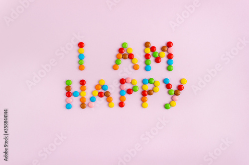 Phrase I am happy made of multi-colored chocolate dragees on pink background. The concept of positive thinking and enjoyment of life.