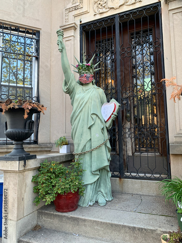 Covid-19 protection mask on a Statue of Liberty and a heart shaped tablet with the writing - Alone together we are one. On a Prospects Lafferts Garden, Brooklyn, NY house stoop.