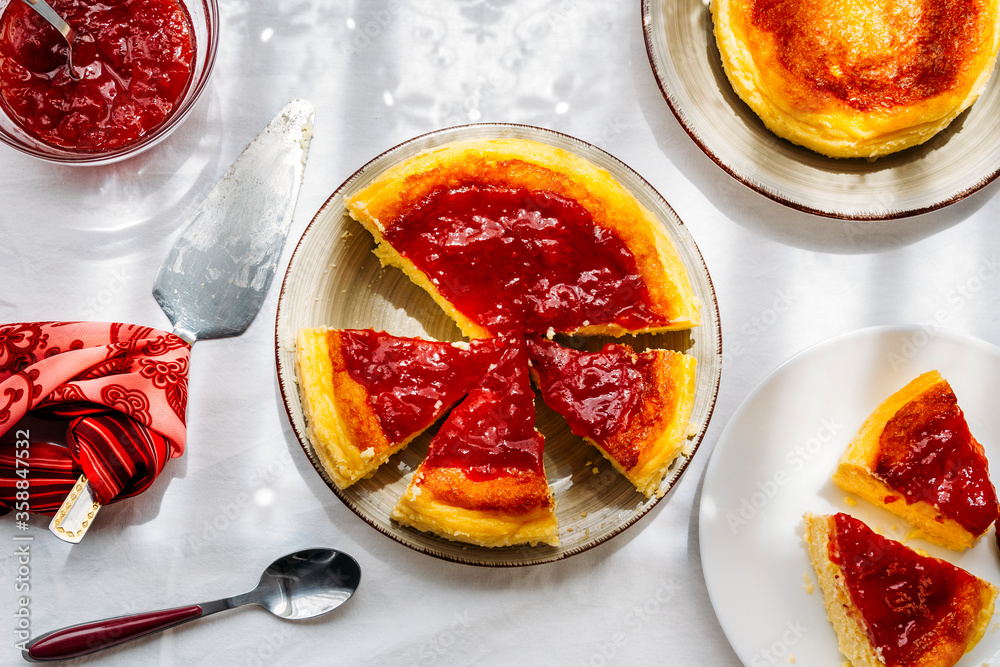 Homemade cheesecake decorated with jam and cut into slices next to a window through which sunshine enters on a warm and sunny day. Healthy, homemade desserts. Homemade cheesecake decorated with jam and cut into slices next to a window through which sunshine enters on a warm and sunny day. Healthy, homemade desserts.
