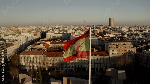 Madrid, Spain. City panorama at sunset, buildings, streets and roofs of houses, view from the top. in the center of the frame the flag of spain soars in the wind