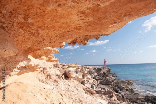 A young woman observes the horizon near a coastal cave. Formentera island, Mediterranean sea, Spain