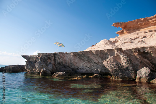 A beach umbrella on a cliff overlooking the sea. Formentera island, Mediterranean sea, Spain