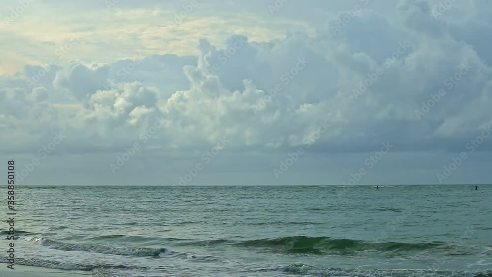 slowly panorama right on large fluffy grey clouds float above blue sea with white waves running to sandy beach in evening summertime slowly panorama right on large fluffy grey clouds float above blue sea with white waves running to sandy beach in evening summertime