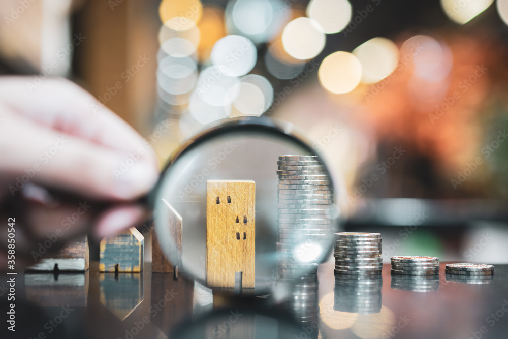 Hand holding magnifying glass and looking at house model, house selection, real estate concept..