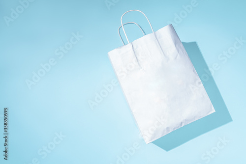 Shopping paper bag. Concept of consumerism, shopping symbol. Copy space trend pastel color. Hard shadows, morning light.