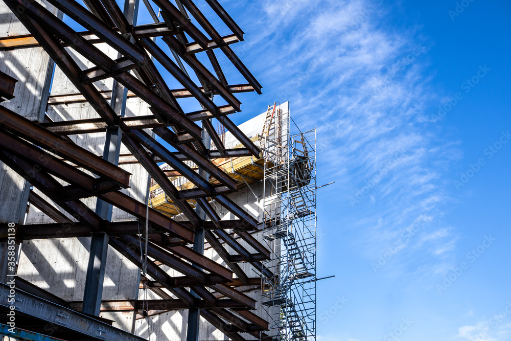Partial construction of an industrial multilevel building. Steel framing /metal beams visible with walkways and ladders. Corner view of half built structure with blue sky. No people.
