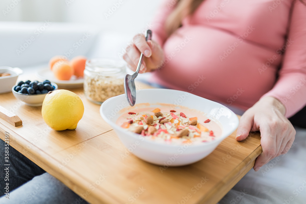 Female sitting on sofa and eating fresh muesli. Pregnancy and healthy lifestyle concept. Female sitting on sofa and eating fresh muesli. Pregnancy and healthy lifestyle concept.