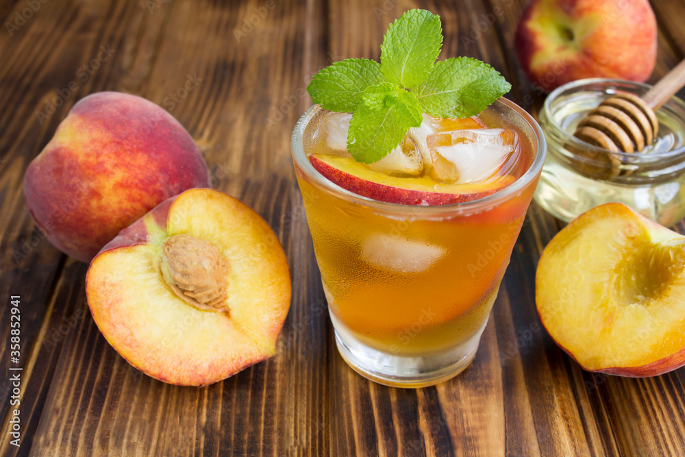 Cold tea with peaches in the glass on the brown wooden background. Closeup. Cold tea with peaches in the glass on the brown wooden background. Closeup.