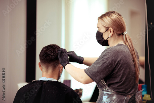 Close up hairdresser with security measures for Covid-19, cuts a man social distance, cutting hair with a medical mask.