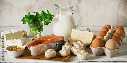 Vitamin D rich foods on a white wooden table, banner. Natural sources of vitamin D are dairy products, salmon, egg, mushrooms, parsley, fish oil.