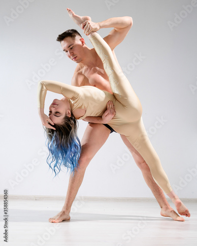 A pair of dancers in action. A young duet of circus artists perform support with twine in the studio. Man in underpants holding Woman in overalls for gymnastics in the splits.