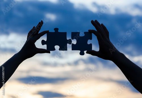 Human hands connecting two jigsaw puzzle pieces against cloudy sky stock photo