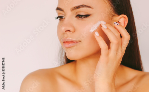 Portrait young sensual beautiful woman with perfect smooth skin apply moisturizing lotion on face isolated on white background. Attractive girl use face cream. Skin care cosmetics, hydration, beauty