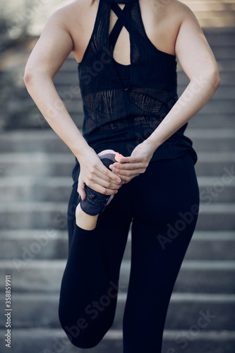 Closeup of attractive fit sportswoman stretching her leg and preparing for running outdoors. City life concept.