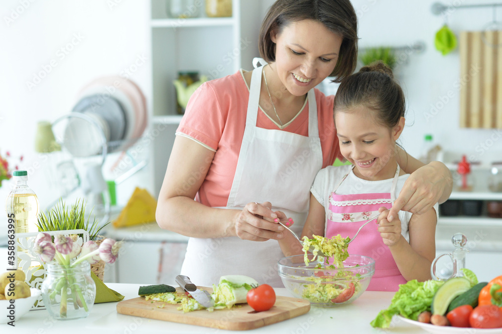 Cute little girl with mother cooking together at kitchen table