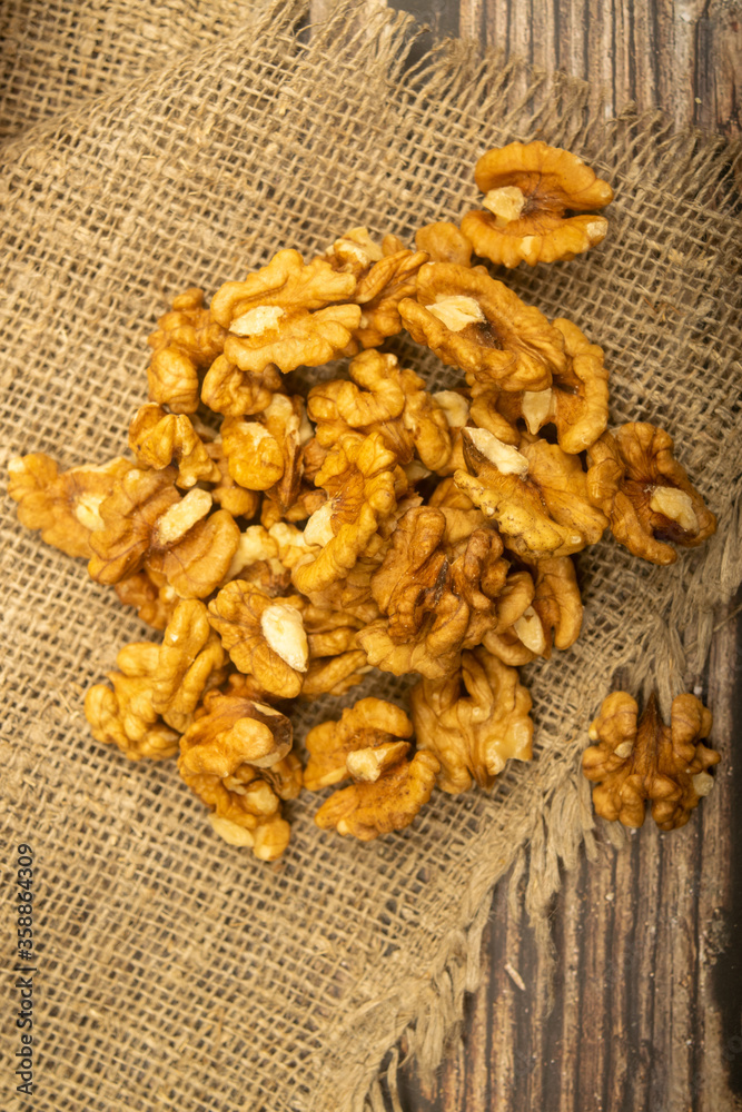 Fototapeta premium Peeled walnuts in bulk on a wooden table covered with rough-textured burlap. Healthy diet. Fitness diet. Close up.